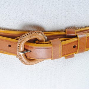 A close-up view of a brown leather belt with a metal buckle, resting on a white surface.