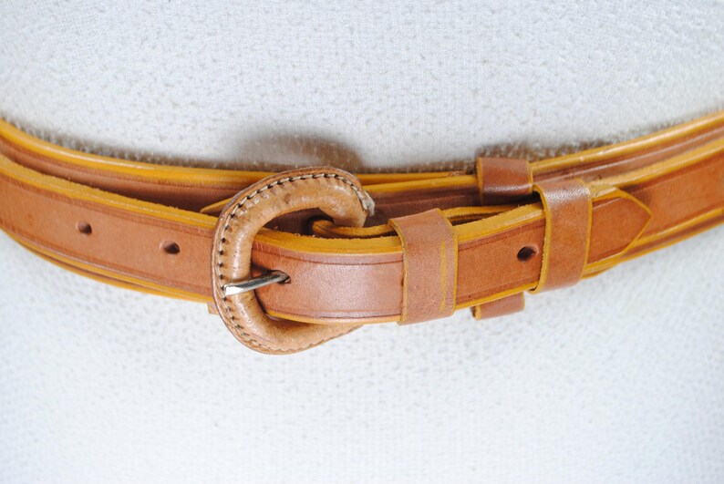 A close-up view of a brown leather belt with a metal buckle, resting on a white surface.