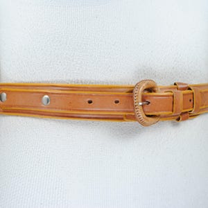 A tan leather belt with a buckle, displayed on a mannequin torso against a white background.