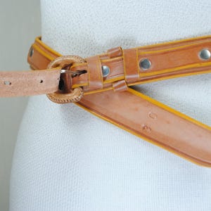 A close-up image of a tan leather belt with a metal buckle, displayed on a mannequin or mannequin head.