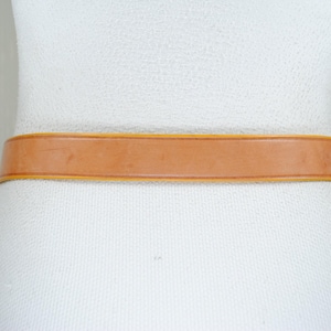 A close-up view of a white mannequin wearing a tan leather belt.