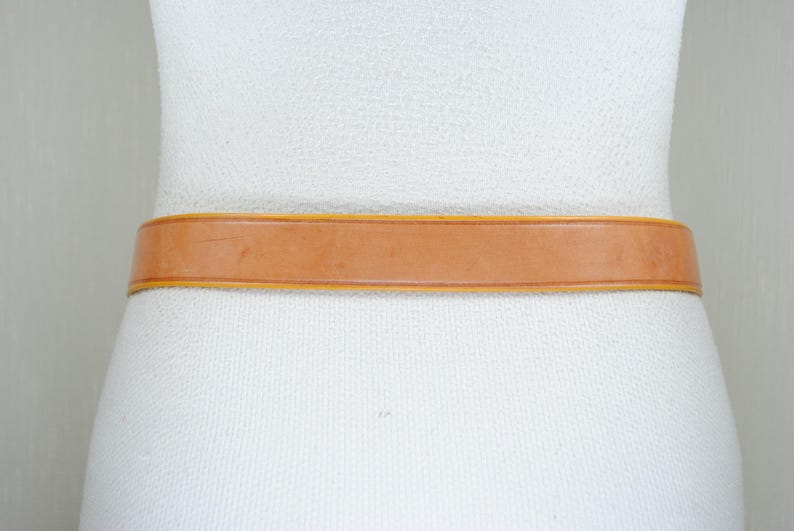 A close-up view of a white mannequin wearing a tan leather belt.