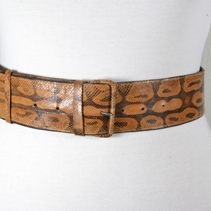 Peut inclure: Une large ceinture en cuir marron avec un motif de peau de serpent et une boucle argentée.