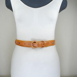 A mannequin wearing a white dress and a brown belt.