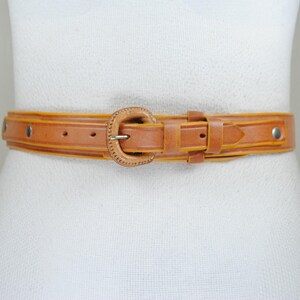 A brown leather belt with a metal buckle is shown on a mannequin.