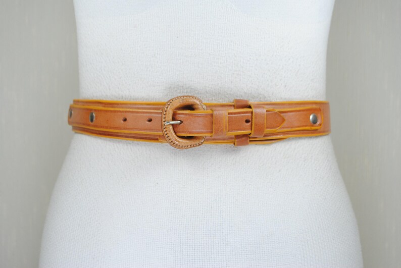 A brown leather belt with a metal buckle is shown on a mannequin.