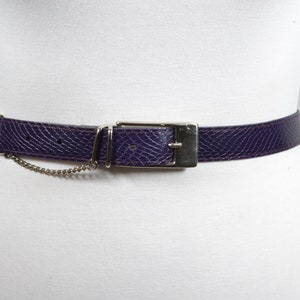 May include: A purple leather belt with a silver buckle and a chain detail.