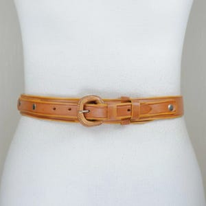 A mannequin wearing a tan leather belt with a metal buckle.