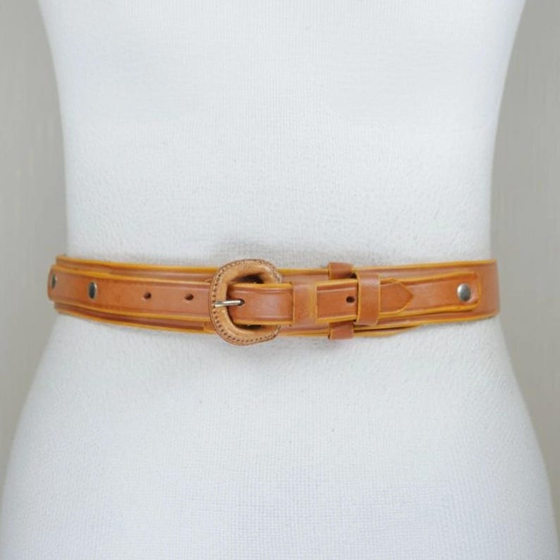 A mannequin wearing a tan leather belt with a metal buckle.