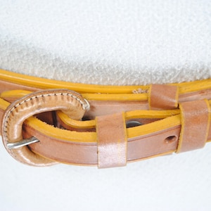 A close-up view of a leather belt with a buckle, showing the details of the belt and the buckle.