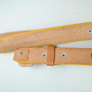 A close-up view of a leather belt with a yellow buckle, showing signs of wear and tear.