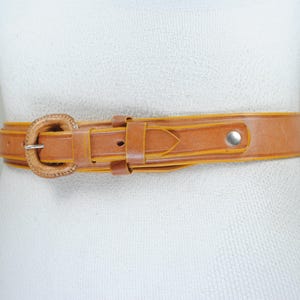 A brown leather belt with a metal buckle is shown on a mannequin.
