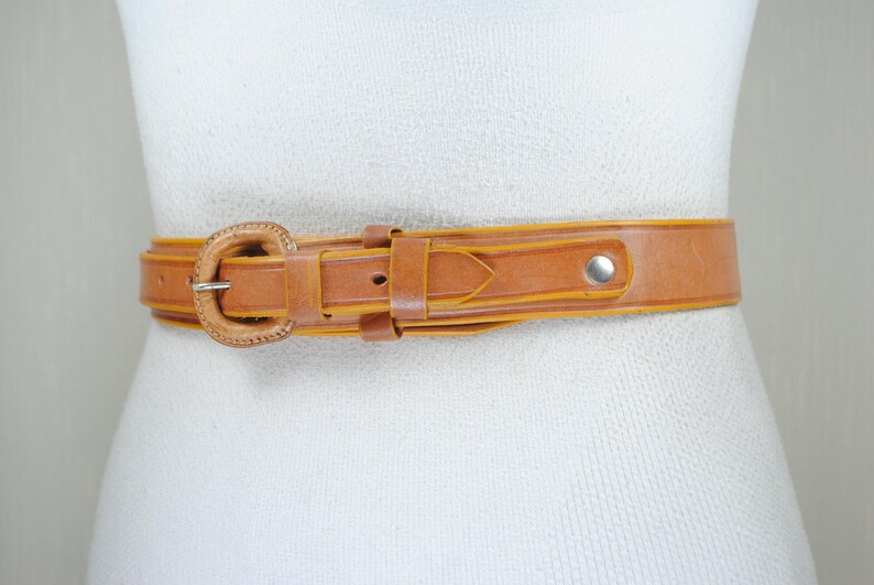 A brown leather belt with a metal buckle is shown on a mannequin.