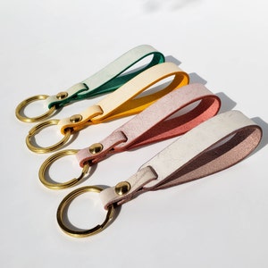 May include: Four leather keyrings with gold key rings. The keychains are in shades of green, yellow, pink, and white.