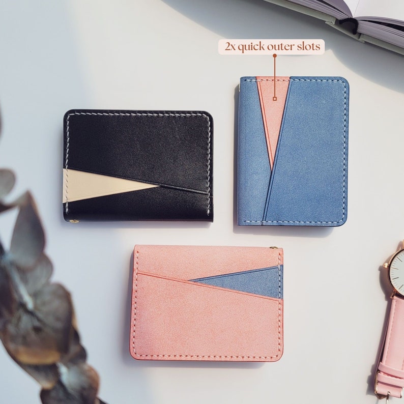 Puede incluir: Tres carteras minimalistas en negro, azul y rosa, cada una con un dise&ntilde;o de bloques de color contrastantes. La cartera negra tiene un acento blanco y beige, la cartera azul tiene un acento rosa y la cartera rosa tiene un acento azul. Las carteras se muestran sobre una superficie blanca.