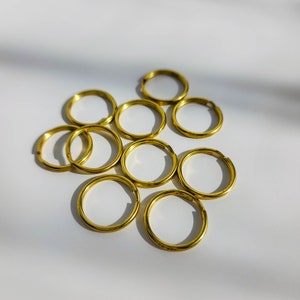 Puede incluir: Un grupo de diez anillos de salto de metal de color dorado. Los anillos est&aacute;n dispuestos en un c&iacute;rculo suelto, con algunas superposiciones.