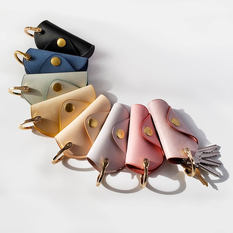 May include: A set of ten leather keychains in various colors, including blue, green, beige, and pink. The keychains are arranged in a semi-circle on a white background.