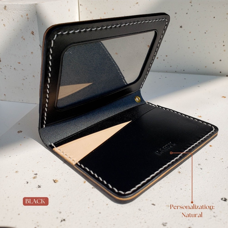 Puede incluir: Cartera de cuero negro con ventana de identificaci&oacute;n transparente y costuras blancas en contraste. La cartera tiene un interior de cuero natural y un remache dorado. La palabra "BLACK" est&aacute; impresa.