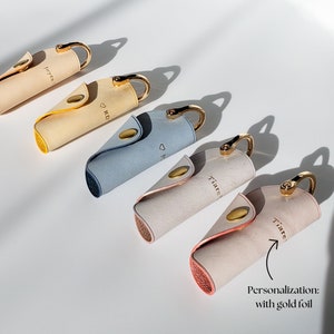 May include: Five leather keyrings with gold rings and personalised gold foil lettering. The keyrings are in various colours, including beige, light blue, and pink.