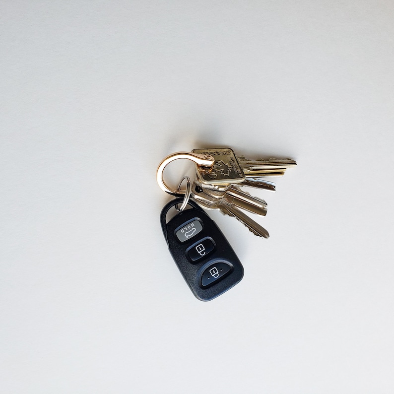 Puede incluir: Un llavero de coche negro con tres botones y un llavero de oro unido a un juego de llaves. Las llaves son doradas y tienen una variedad de formas y tama&ntilde;os.