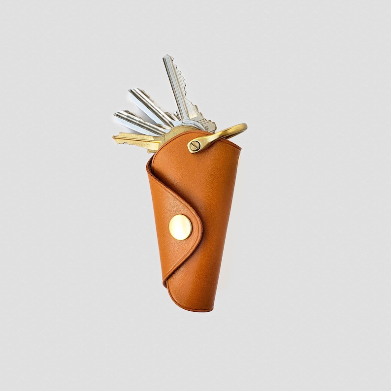 May include: A brown leather key holder with a brass snap closure and a set of keys inside.