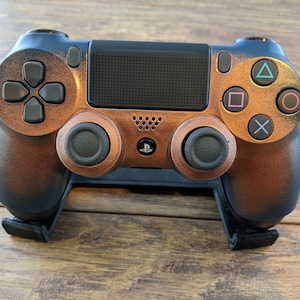 May include: A black and copper colored PlayStation 4 controller with a textured finish. The controller is on a black stand.