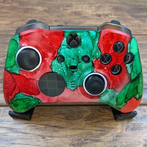 May include: A custom-painted Xbox controller with a red, green, and white abstract design. The controller has a black faceplate and black buttons.