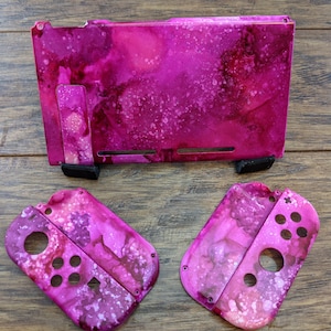 May include: A set of three pink and white Nintendo Switch console and Joy-Con controller faceplates with a marbled design.