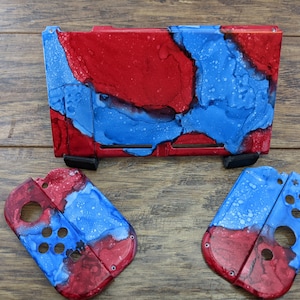 May include: A set of three Nintendo Switch console covers featuring a red, white, and blue abstract design. The covers are made of durable plastic and are easy to install.