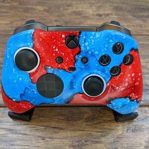 May include: A custom-painted Xbox controller with a blue and red abstract design. The controller has black buttons and a black D-pad.