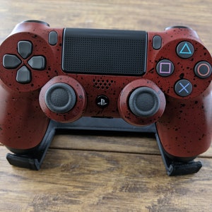 May include: A red and black PlayStation 4 controller with a speckled paint design. The controller is on a black stand.