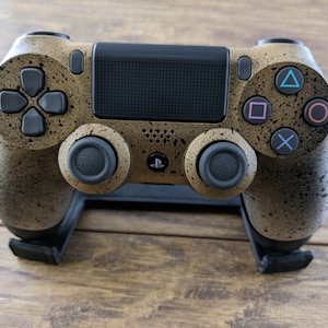 May include: A gold-colored PlayStation 4 controller with a speckled finish. The controller is on a black stand and features the standard PlayStation buttons.