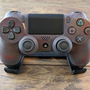 May include: A gray and red PlayStation 4 controller with a distressed paint finish. The controller is on a black stand.
