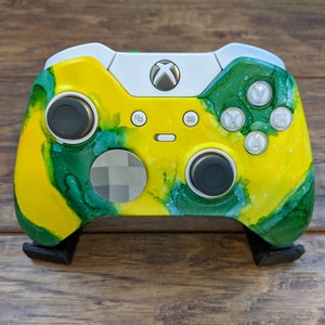 May include: A custom-painted Xbox controller with a yellow and green abstract design. The controller has black buttons and a white faceplate.