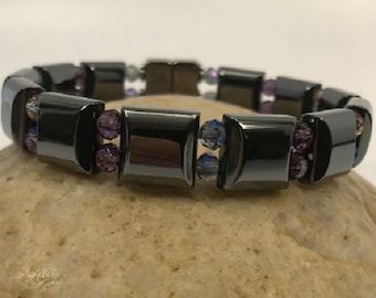 May include: A black hematite bracelet with purple and blue crystal beads. The bracelet is made of square-shaped hematite beads and is strung on elastic.