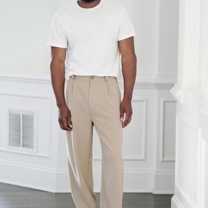 K&ouml;nnte beinhalten: Eine Person tr&auml;gt ein wei&szlig;es T-Shirt und eine beige Bundfaltenhose. Die Person tr&auml;gt au&szlig;erdem eine Brille und Turnschuhe. Das Outfit ist ein l&auml;ssiger, allt&auml;glicher Stil.