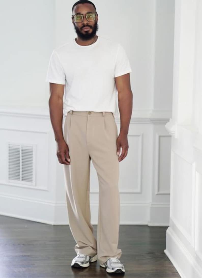 K&ouml;nnte beinhalten: Eine Person tr&auml;gt ein wei&szlig;es T-Shirt und eine beige Bundfaltenhose. Die Person tr&auml;gt au&szlig;erdem eine Brille und Turnschuhe. Das Outfit ist ein l&auml;ssiger, allt&auml;glicher Stil.