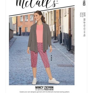 May include: A sewing pattern for a women's outfit, featuring a long-sleeved cardigan, a pink top, and cropped pants. The pattern is from McCall's and is designed by Nancy Zieman. The model is wearing the outfit and standing on a cobblestone street.