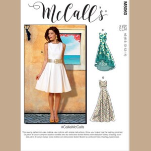 May include: A McCall's sewing pattern featuring a woman in a white dress with a gold belt. The pattern includes multiple dress styles. The text "McCall's" is at the top, and the pattern number M8060 is on the right.