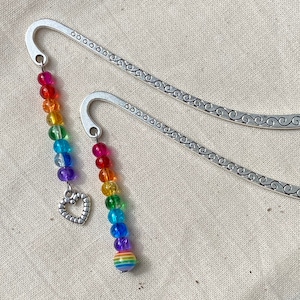 Op de afbeelding: Twee zilveren bladwijzers met een regenboog kralenbedel. De bedels hebben een hart en een regenboog gestreepte kraal aan het einde.