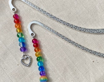 Könnte beinhalten: Zwei silberne Lesezeichen mit einem Regenbogen-Perlen-Anhänger. Die Anhänger haben ein Herz und eine regenbogenfarbene Perle am Ende.