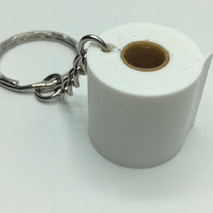 May include: A keychain featuring a miniature white toilet paper roll charm. The charm has a cylindrical white body with a hollow tan center core. A silver-toned metal chain and a circular split ring are attached to the top of the toilet paper roll.