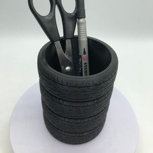 May include: Black tire-shaped pencil holder with a silver pen and black scissors inside.
