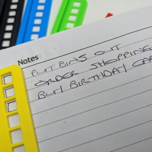 May include: A yellow notepad with a checklist and the handwritten text "Put bins out, Order shopping, Buy birthday card".