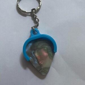 May include: A blue guitar pick holder with a silver key chain attached. The pick is made of iridescent mother of pearl.