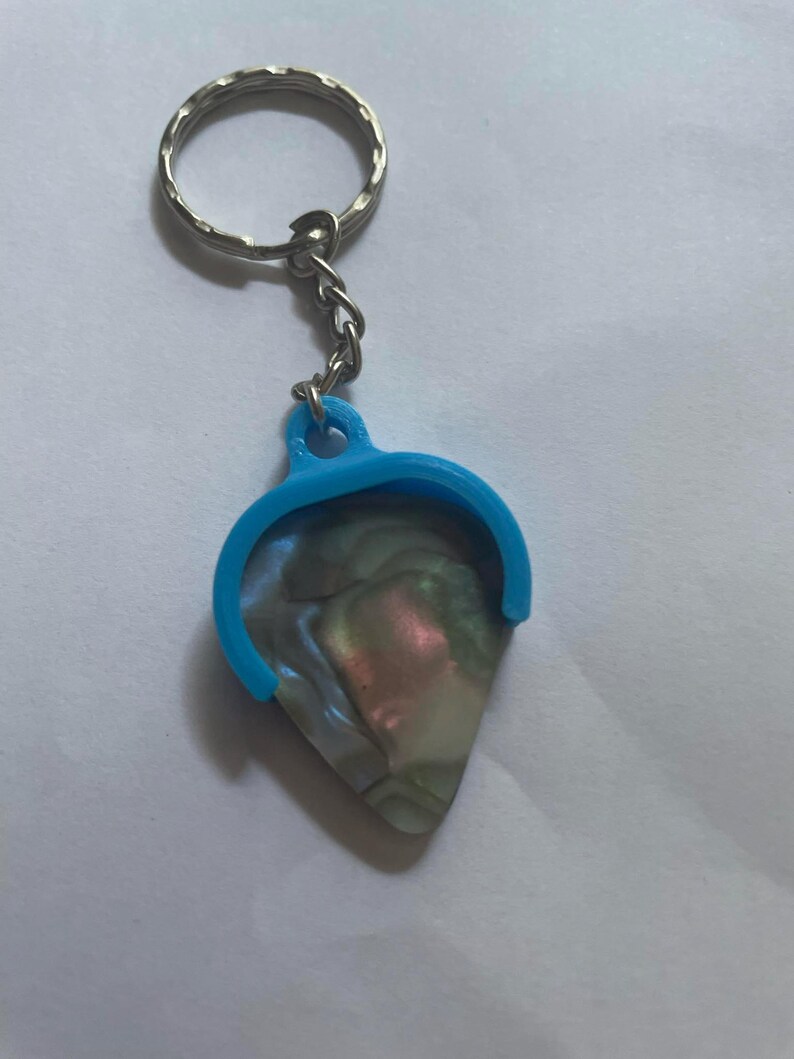 May include: A blue guitar pick holder with a silver key chain attached. The pick is made of iridescent mother of pearl.