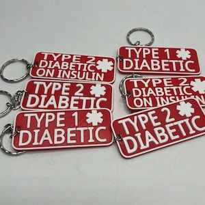 May include: Red and white rectangular keyrings with the words "TYPE 1 DIABETIC" and "TYPE 2 DIABETIC" in white lettering. Some keyrings also read "ON INSULIN". Each keyring has a silver keyring attached.