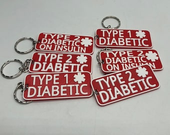 Puede incluir: Una colección de llaveros rectangulares rojos con texto blanco y un símbolo de estrella médica blanco. Los llaveros presentan varias inscripciones que incluyen TYPE 1 DIABETIC, TYPE 2 DIABETIC y TYPE 2 DIABETIC ON INSULIN, unidos a una anilla.