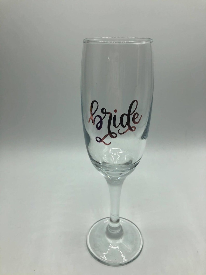 May include: A clear glass champagne flute with the word "bride" written in gold lettering.