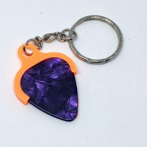 May include: A purple guitar pick keychain with an orange holder and a silver key ring.